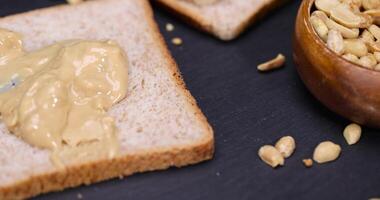 peanut butter on a piece of bread and roasted peanuts on the table photo