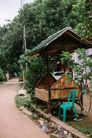 Rustic bamboo structure with green roof and a plastic chair by the roadside photo
