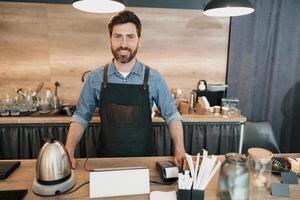 Portrait of smiling Barista with stylish beard while behind a counter in the coffeeshop photo