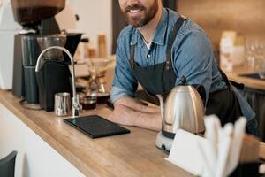Close up of barista with stylish beard smiling while behind a counter in coffeeshop photo
