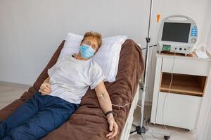 Sick patient in mask lying in hospital ward during medical procedure in clinic photo