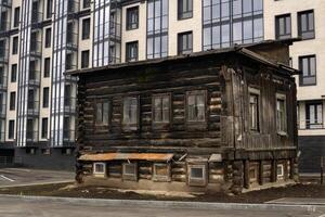old log house was not demolished to be used as a utility room during the construction of a multi-story modern building photo