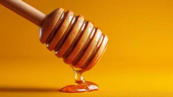Honey dripping from a wooden honey dipper against a vibrant orange background photo