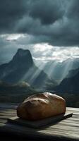 Loaf of bread on wooden table with dramatic mountain backdrop and sun rays photo