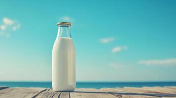 Glass bottle of milk on wooden table against clear blue sky and sea background photo