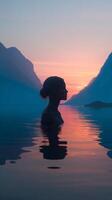 Silhouette of a woman in water with vibrant sunset reflecting in mountains photo