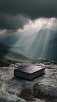 Mystical book on rocky mountain under dramatic sky with sun rays, fantasy concept photo