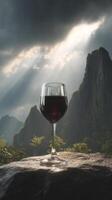 Glass of red wine on stone with sun rays through mountain clouds, serene landscape photo