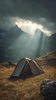 Sun rays breaking through dark clouds onto a tent in a serene mountain valley photo