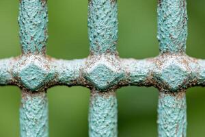 of a weathered, light teal colored metal fence. A detailed view of the intricate design and rust marks on the fence's crossbars. A captivating glimpse into the beauty of aged structures. photo