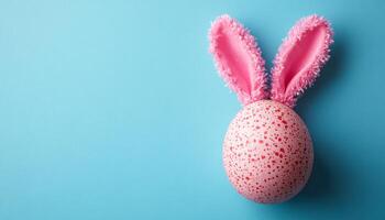 Bunny-eared egg on blue bg. A decorated Easter egg with pink fluffy bunny ears sits on a bright blue background, adding festive charm. photo