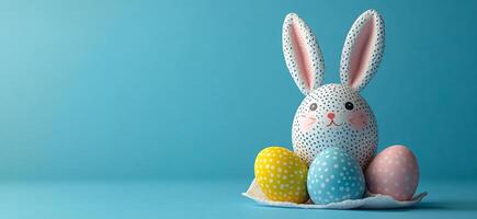 Bunny and eggs on table. A cheerful bunny decoration is surrounded by pastel-colored, polka-dotted eggs on a blue backdrop. photo