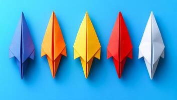 Colorful paper planes arranged in a row. Five colorful paper planes are lined up against a blue background, showcasing playfulness and creativity. photo
