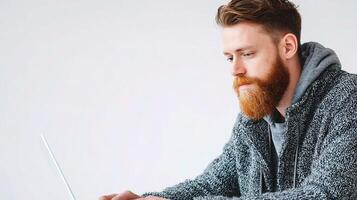 A man with a beard and red hair is using a laptop photo