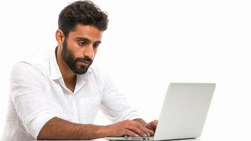 A man with a beard and white shirt is sitting at a table with a laptop photo