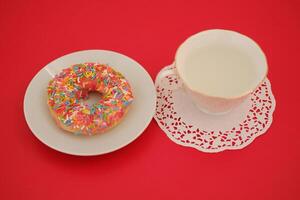 a delightful snack setting featuring a pink-frosted donut covered in colorful rainbow sprinkles, served on a white plate photo