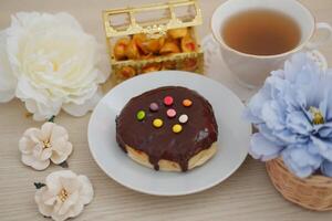 a delicious chocolate-glazed donut topped with colorful candy sprinkles, placed on a white plate photo