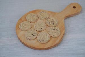 nine round cookies neatly arranged on a small wooden serving board with a handle photo