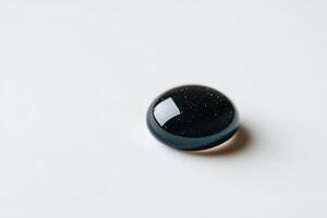 Glistening black droplet resting on a smooth white surface, showcasing subtle reflections photo
