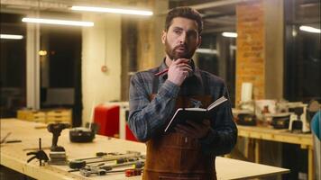 Thoughtful Caucasian man guy wood master builder thinking writing copybook in workshop puzzled carpenter pondering problem designer creating plan difficulty male brainstorm craftsman raise finger idea video