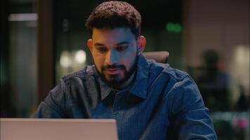 Thoughtful businessman Indian man business worker thinking plan computer online browsing in night evening office overtime working male entrepreneur IT company laptop programmer think idea inspired video