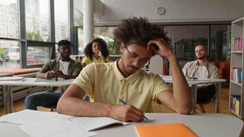 African American man student guy writing task in class lesson in classroom friends classmates bullying mocking bully throwing papers balls mockery laughing four students lecture in university college video