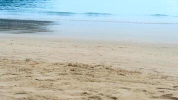 Front is a blurry image of feet floating on the sand. Focus on the center of the smooth sandy beach. Calm water surface and waves. photo
