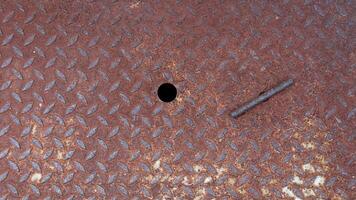 Close up of a rusty metal Lid plate. Raised textured pattern of Lid provides a non slip surface. See the steel rods for pulling the pipe and the ventilation holes. photo