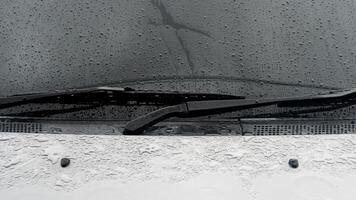 Car gray color covered with raindrops. Focus on two old black wiper blades. Background of car windshield with raindrops flowing down. photo