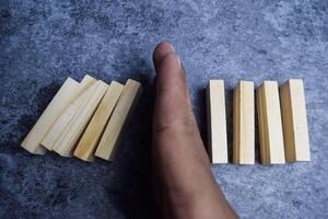 Hand of a businessman stopping domino effect on wooden blocks photo