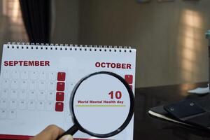 Magnifying glass in hand on calendar with text world mental health day on 10 october. Concept of a public realtions campaign photo