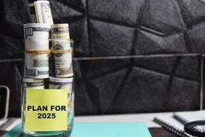 Concept of Plan for 2025 write on sticky notes with dollars in glass jar photo