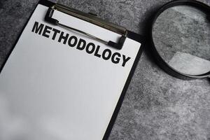 Concept of Methodology write on paperwork with a magnifier isolated on Wooden Table. photo
