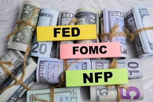 Concept of FED - FOMC - NFP write on sticky notes with dollars isolated on Wooden Table. photo