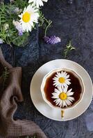 A single daisy floats in the dark tea within the cup. photo
