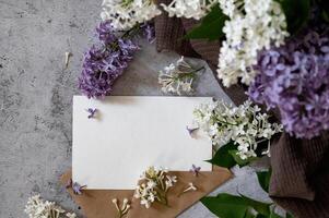 Composition with empty purple envelope and beautiful spring lilac flowers on blue background. Mockup card invitation greeting card postcard copy space template. Branches of lilac blooming bouquet. photo