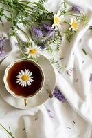 The image features a cup of tea surrounded by wildflowers on a white linen surface. photo