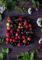 Fresh berries. Red currants, blackberries, blueberries and raspberries in bowls on a large wooden board with mint leaves, strawberries and pomegranate seeds. Background image, top view, vertical photo