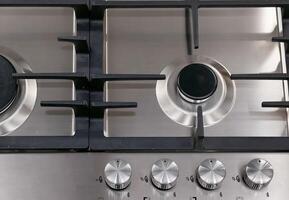 Front view of Contemporary tempered glass gas stove hob with Two burners with auto ignition knob on wooden countertop, cast iron pan supports fan hood and oven built in compact photo