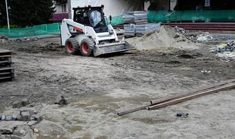 A small tractor works in the sand, filling up a hole. Shovels are on the ground. View from above. photo
