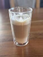 Large transparent mug with Dalgona coffee. Nicely and neatly laid out whipped coffee foam in cold milk. Dalgona, coffee beans, milk bottle, sugar bowl and cinnamon sticks on a light background photo
