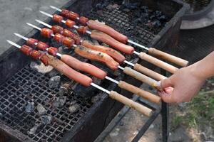 female hand frying sausages on skewers on grill. photo