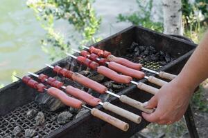 hand frying sausages on skewers on grill. photo