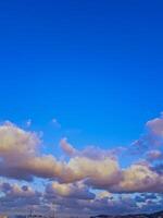 Rugs of rugged clouds drift across the upper half of the horizon, casting a soft glow on the urban scene and natural beauty, while the front sky remains clear and blue. photo