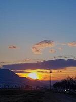 As the sun sets, a breathtakingly picturesque scene unfolds, bathing the landscape in a warm, golden light that emanates from the horizon, nestled between rugs of clouds. photo