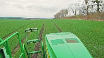 View from tractor cab over green crop rows on farmland, Agricultural field with tire tracks and distant tree line video