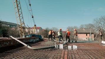 Close-up of construction workers directing concrete hose with safety gear and crane wires in background video