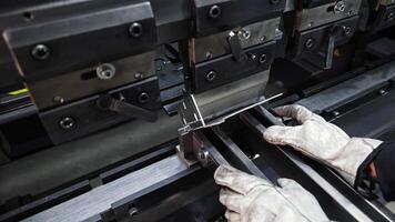 Worker operating press brake to bend sheet metal component, Precision metal forming with gloves in industrial workshop video