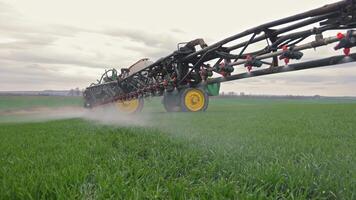 Tractor-mounted sprayer dispersing fertilizer mist over wide green field, Agricultural machine in open farmland with extended boom video