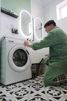 man doing laundry in the bathroom loading washer with clothes photo